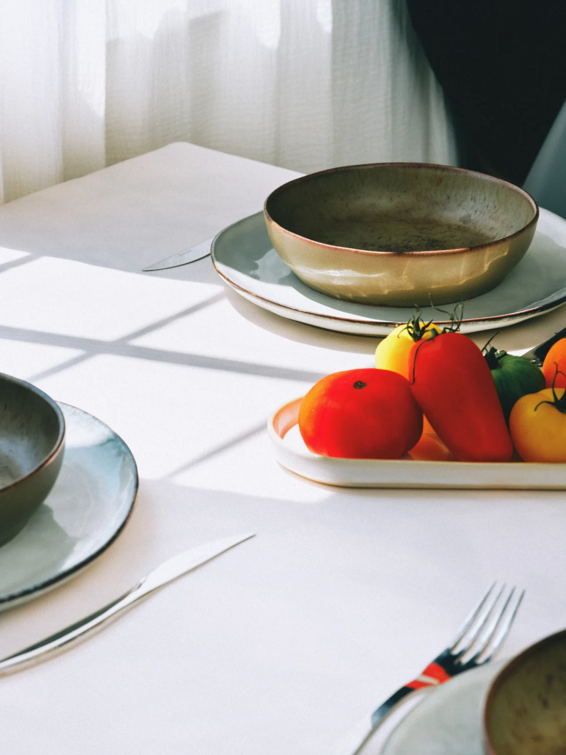 Vaisselle verte et légumes sur une table blanche éclairée par le soleil.