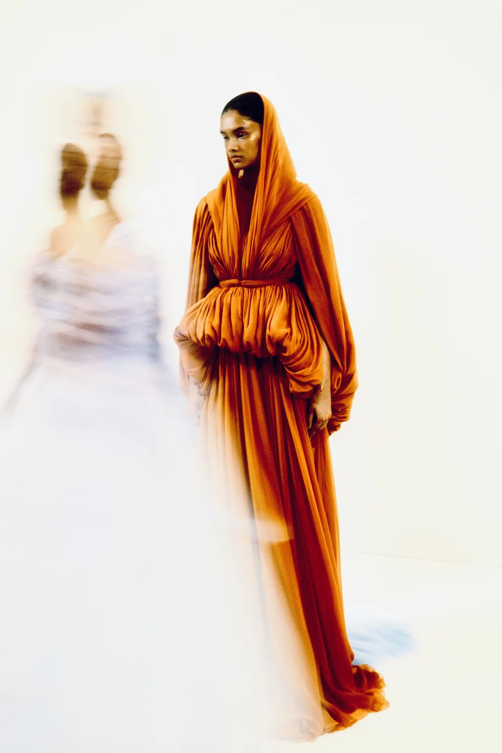 Mannequin portant une tenue orange sur un podium de défilé.