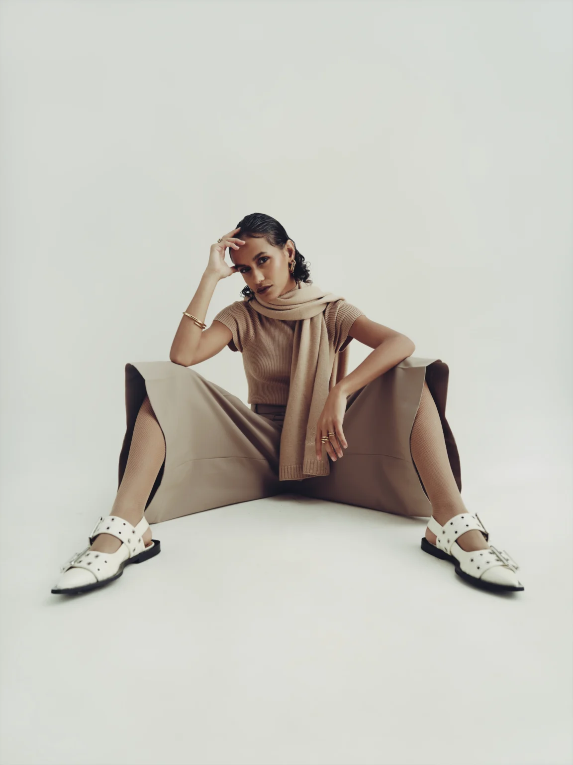 Femme assise dans une pose ample portant une tenue beige et des baskets.