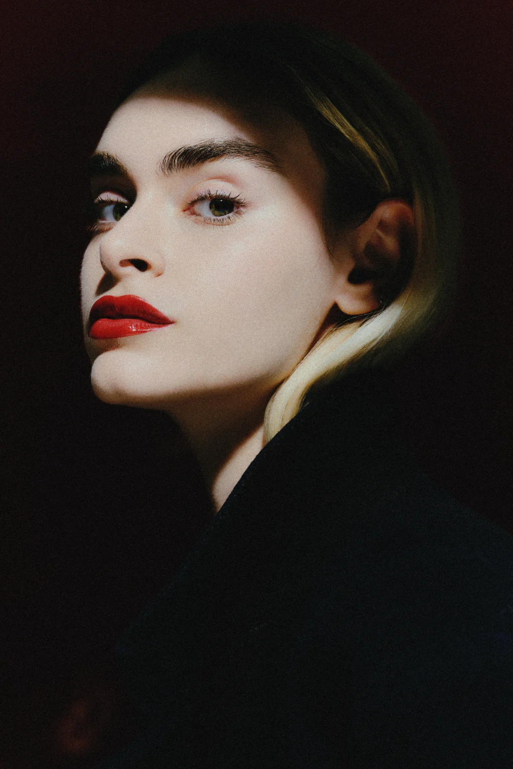 Portrait d’une femme aux lèvres rouges sur fond sombre.