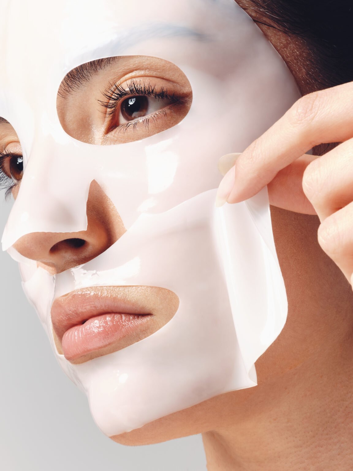 Femme ajustant un masque de soin blanc sur son visage.