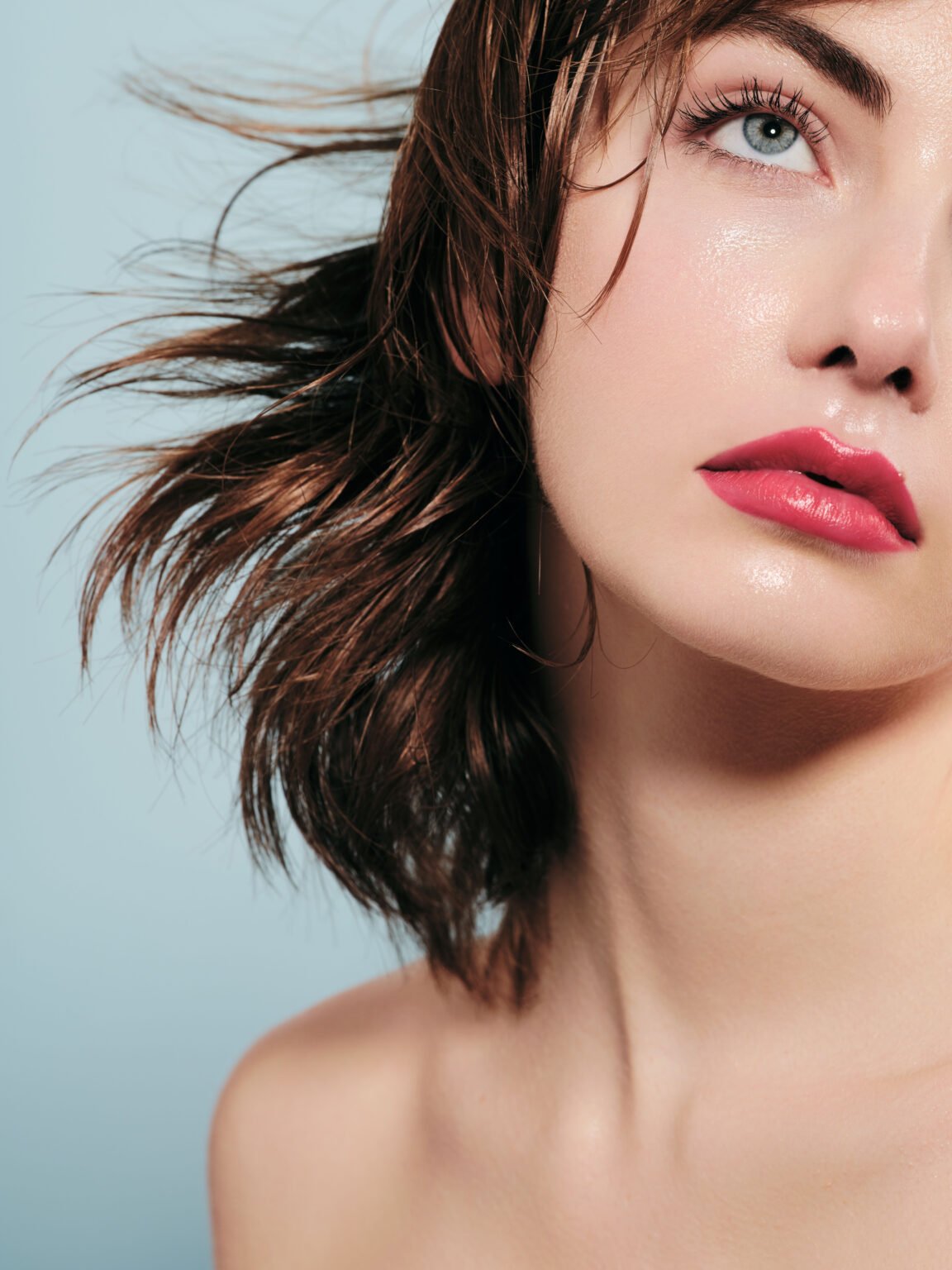 Portrait beauté d’une femme brune aux lèvres roses sur fond bleu clair.