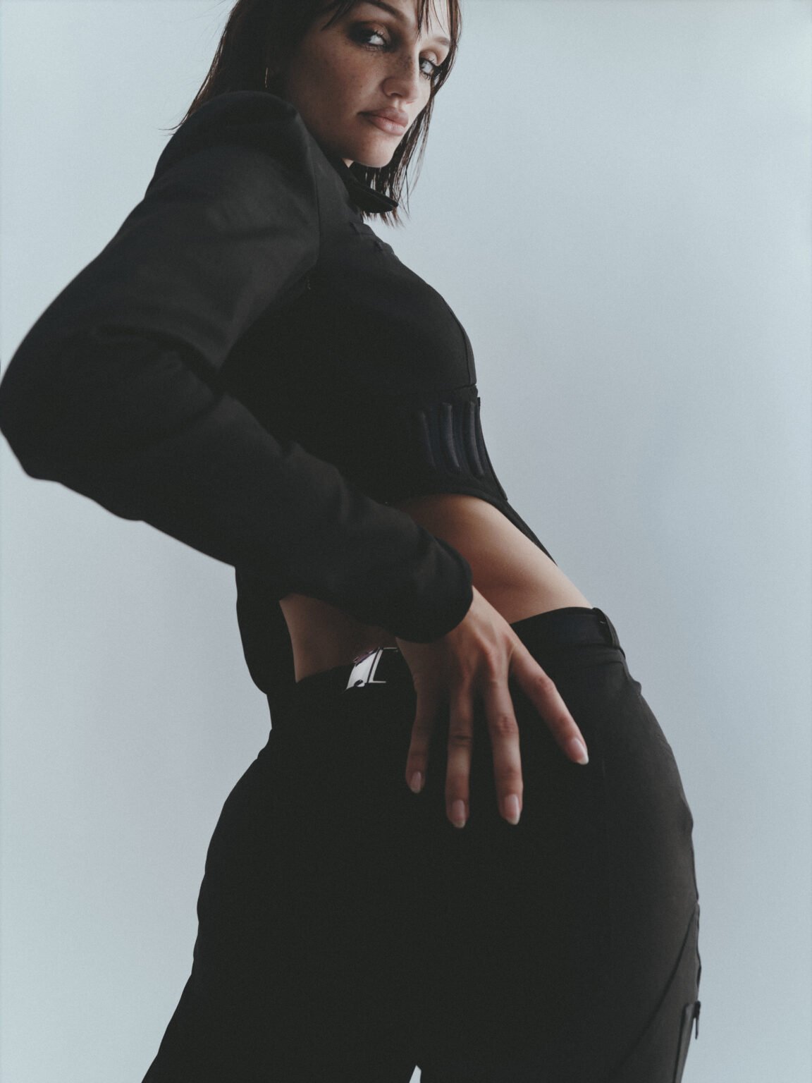 Femme de profil en tenue noire avec une main sur la hanche.