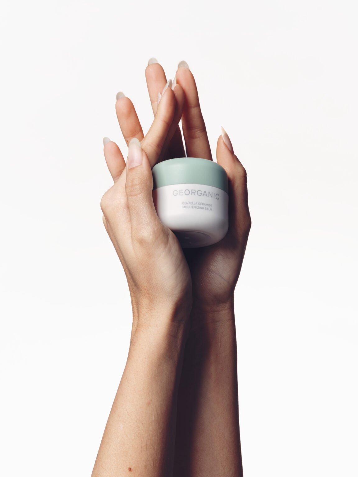 Mains présentant un pot de soin cosmétique sur fond clair.